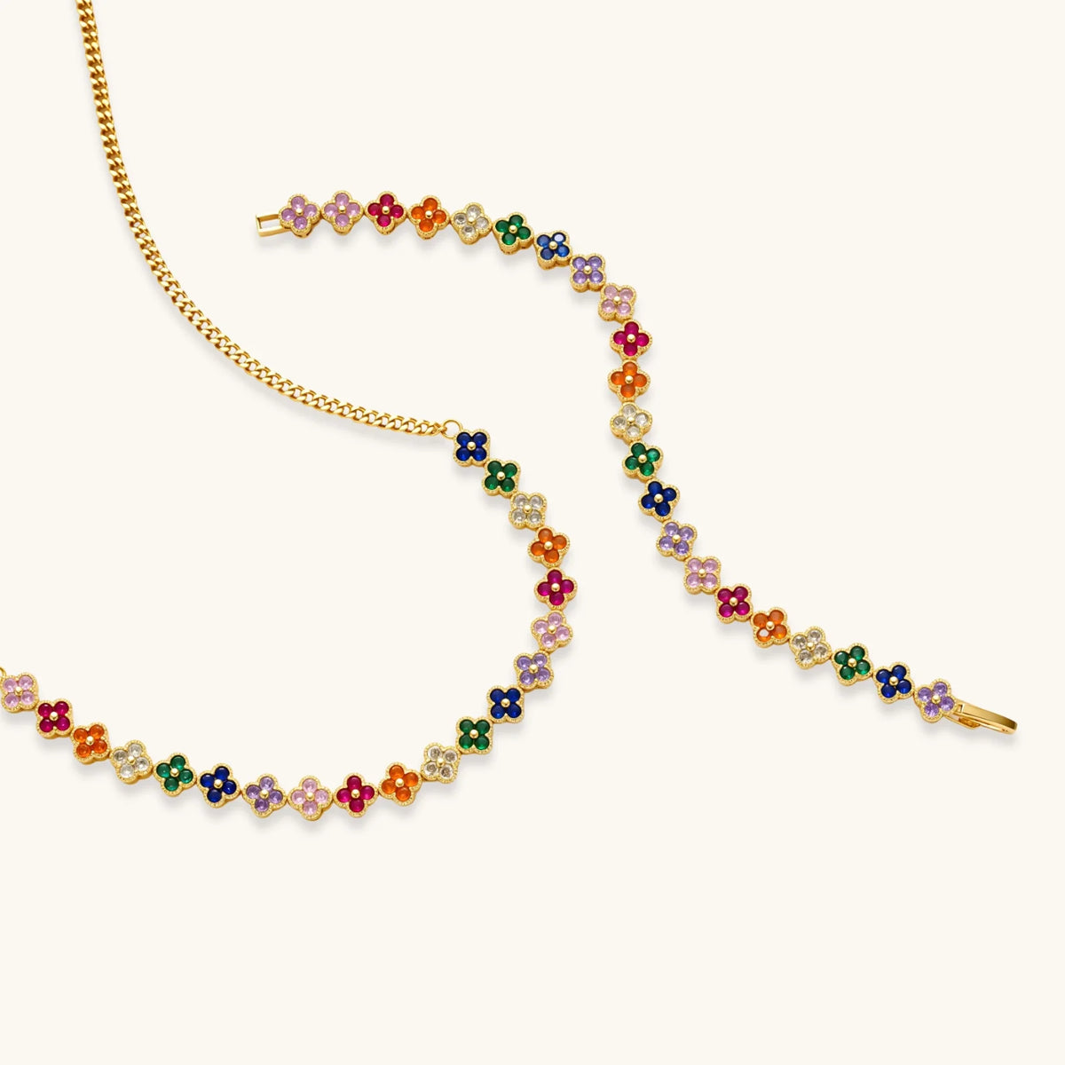 Colorful four-leaf clover jewelry set with rainbow cubic zirconia stones in gold-plated setting on white background