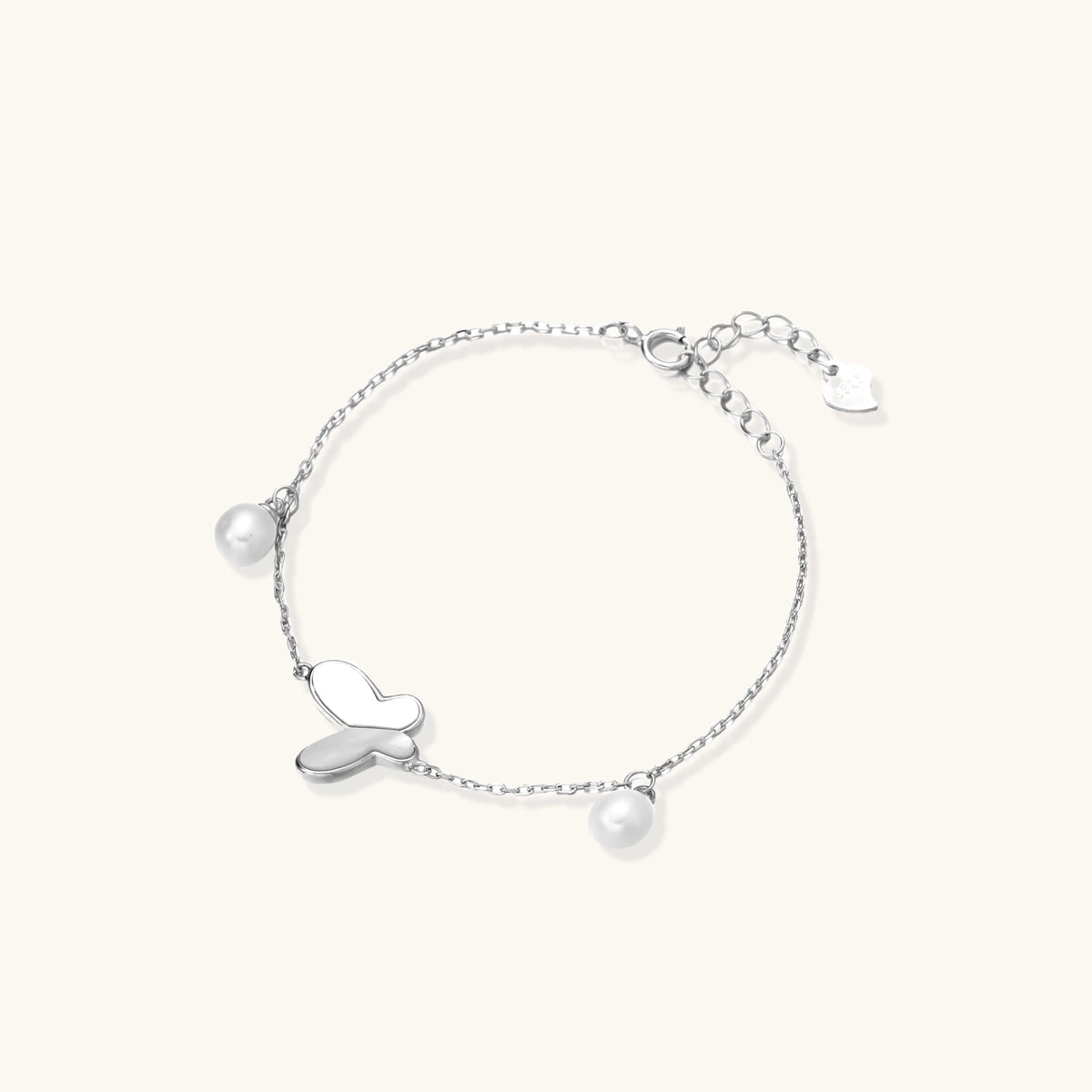Delicate rhodium-plated silver chain bracelet with butterfly charm and two freshwater pearls on cream background
