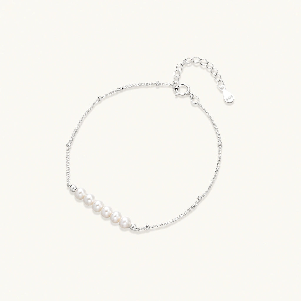 Delicate rhodium-plated silver chain bracelet with row of small baroque pearls centered on white background.