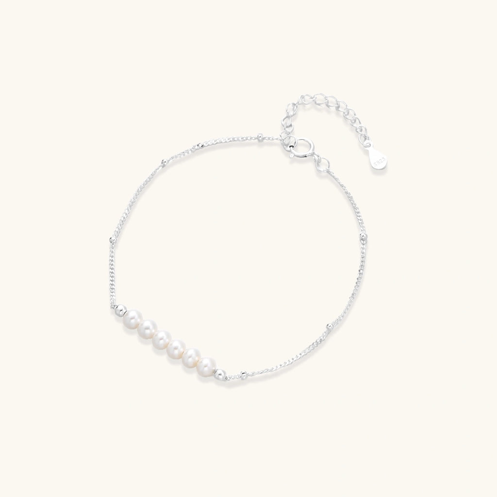 Delicate rhodium-plated silver chain bracelet with row of small baroque pearls centered on white background.