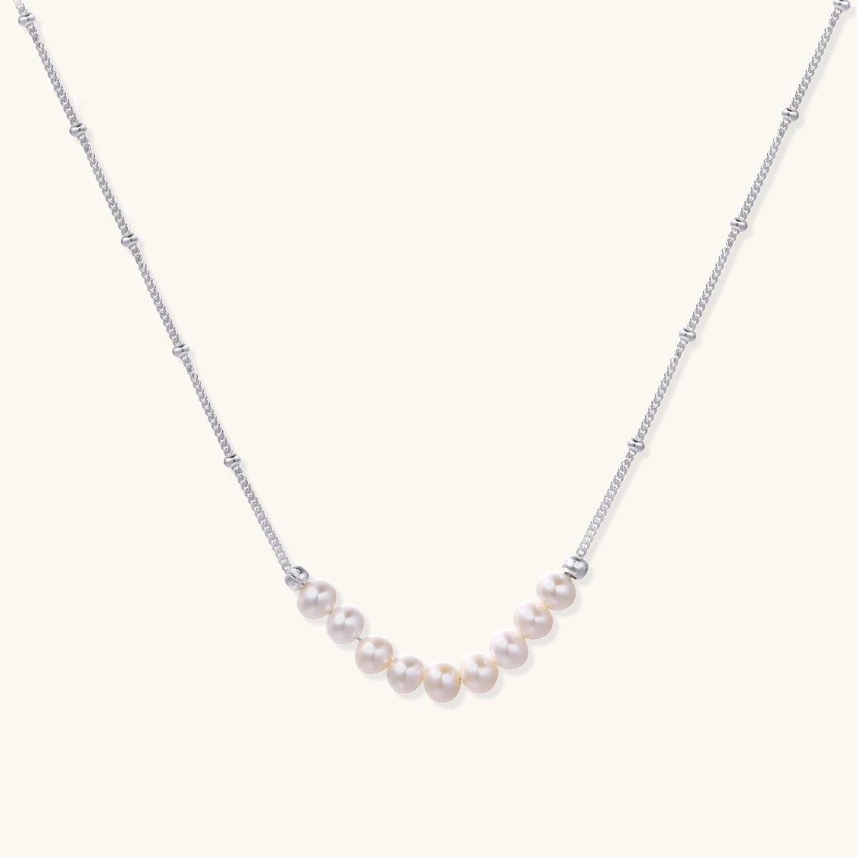 Delicate sterling silver chain necklace with small freshwater pearls arranged in a curved smile arc on cream background.