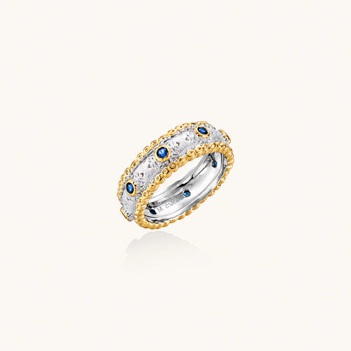 Two-tone ring with brushed silver center, gold beaded edges, and blue zirconia stones on white background.
