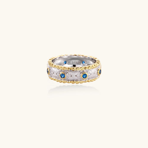 Two-tone ring with brushed silver center, gold beaded edges, and blue zirconia stones on white background.