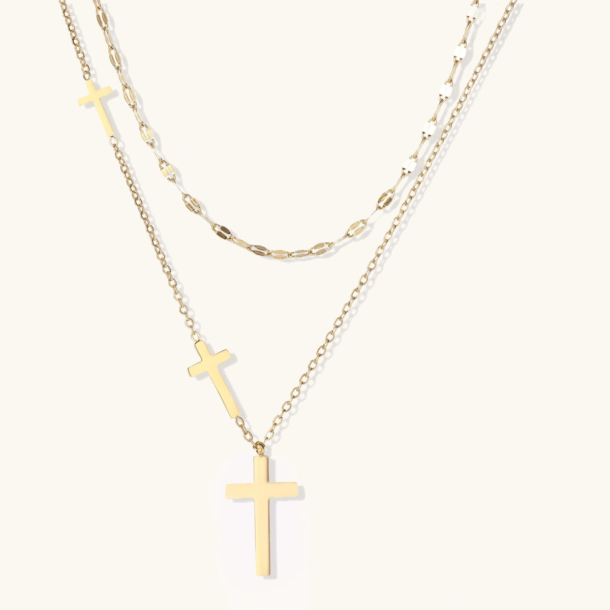 Three-layered gold necklace set with graduated cross pendants in mixed chain styles on white background.