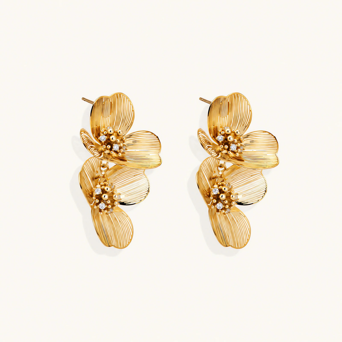 Pair of gold-plated double flower earrings with textured petals and crystal centers on cream background.