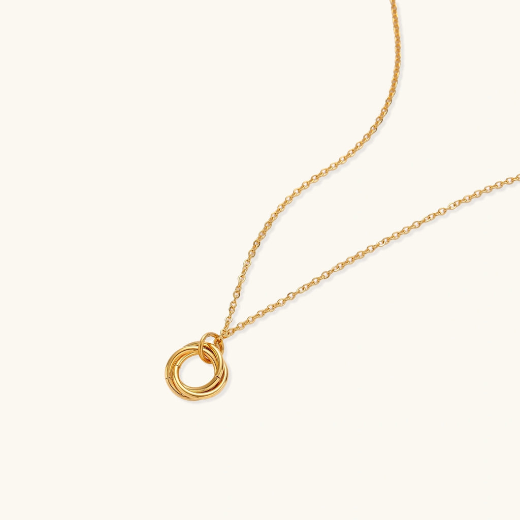 Delicate gold-plated necklace with three interlocking circle rings forming a minimalist knot pendant on cream background