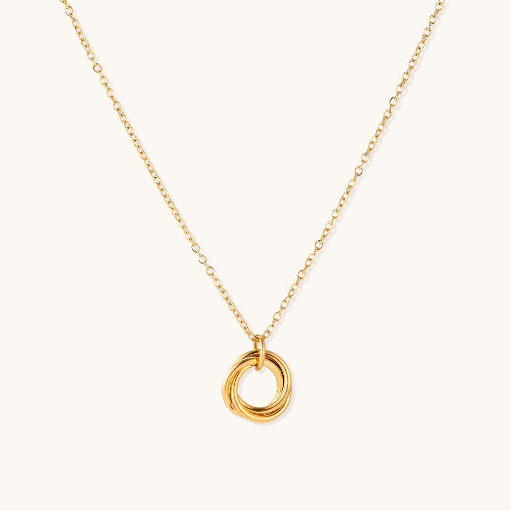 Delicate gold-plated necklace with three interlocking circle rings forming a minimalist knot pendant on cream background