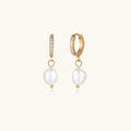 Gold huggie hoop earrings with pavé crystals and white freshwater pearl drops on cream background