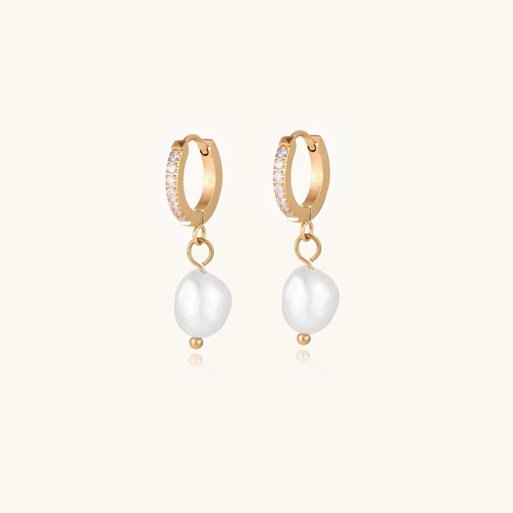 Gold huggie hoop earrings with pavé crystals and white freshwater pearl drops on cream background