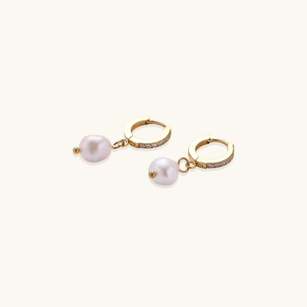 Gold huggie hoop earrings with pavé crystals and white freshwater pearl drops on cream background