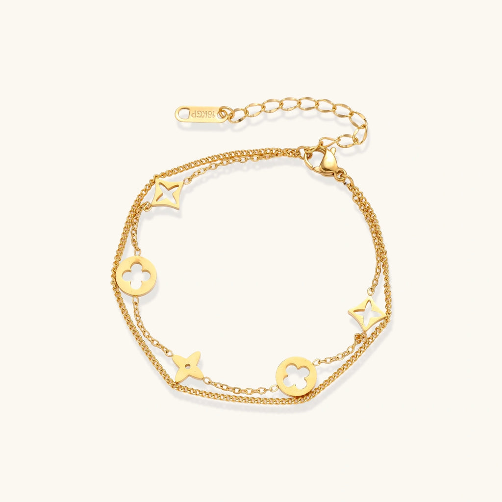 Double-layer gold-plated bracelet with quatrefoil and star charms on cream background, 18K gold finish.