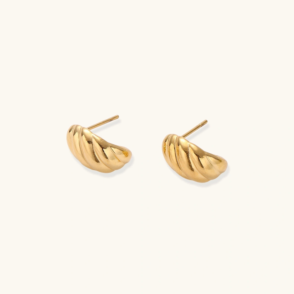 Chunky gold twisted rope huggie hoops with diagonal grooves and high-polish finish on cream background