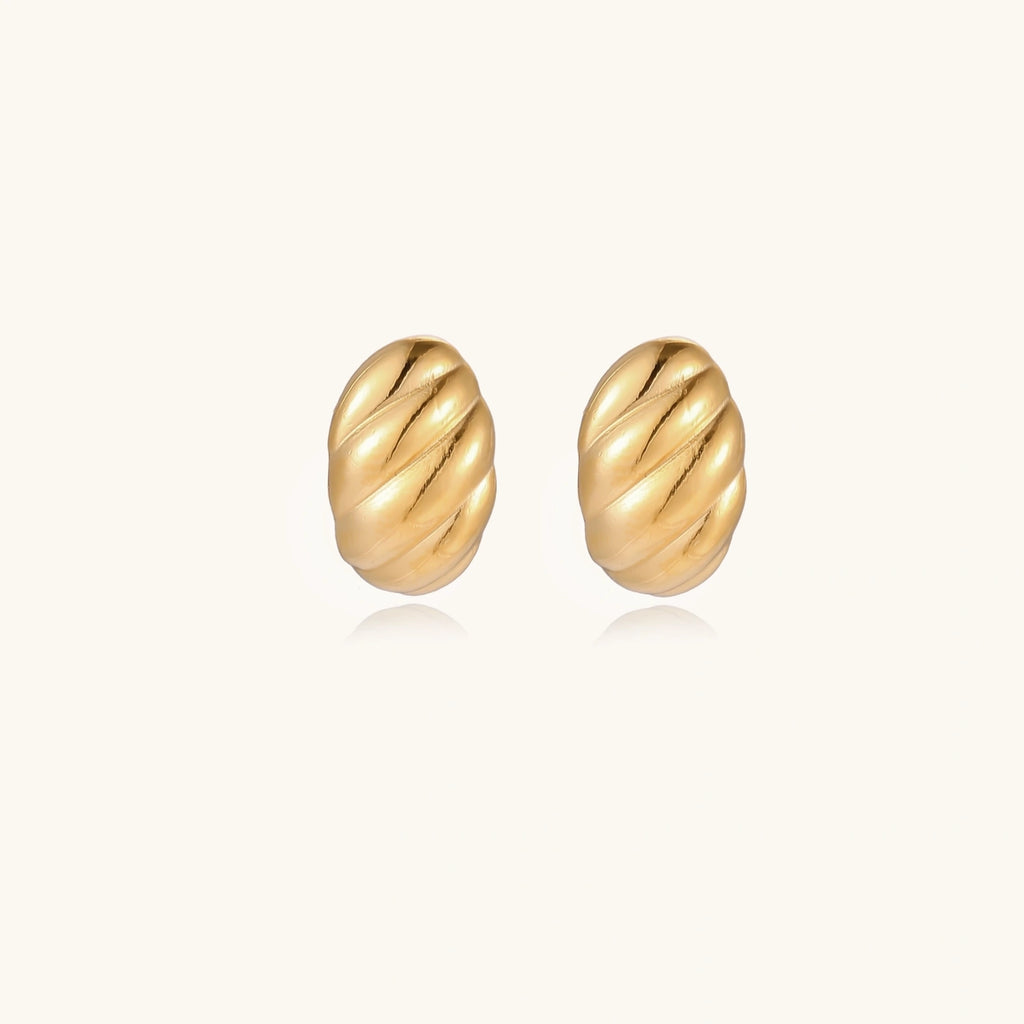 Chunky gold twisted rope huggie hoops with diagonal grooves and high-polish finish on cream background