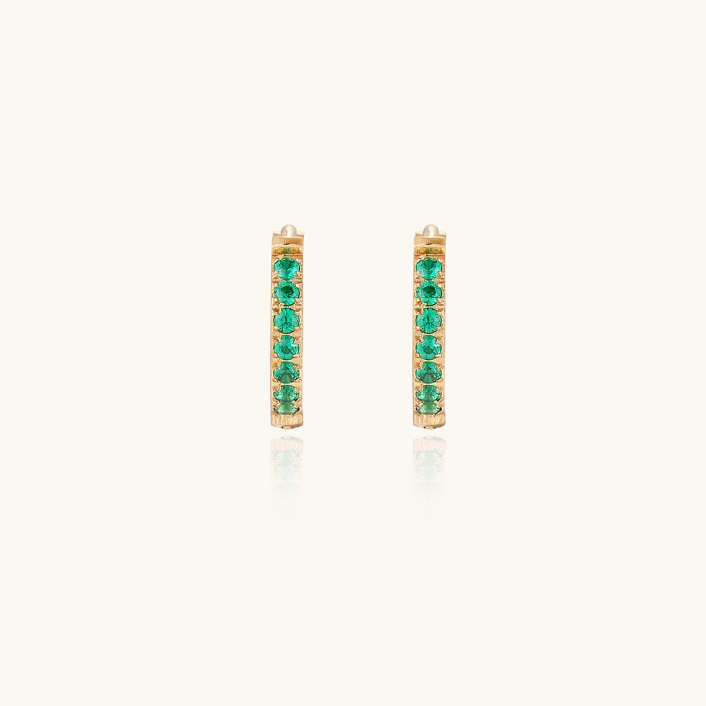 Pair of small gold huggie hoop earrings with bright green cubic zirconia stones on cream background