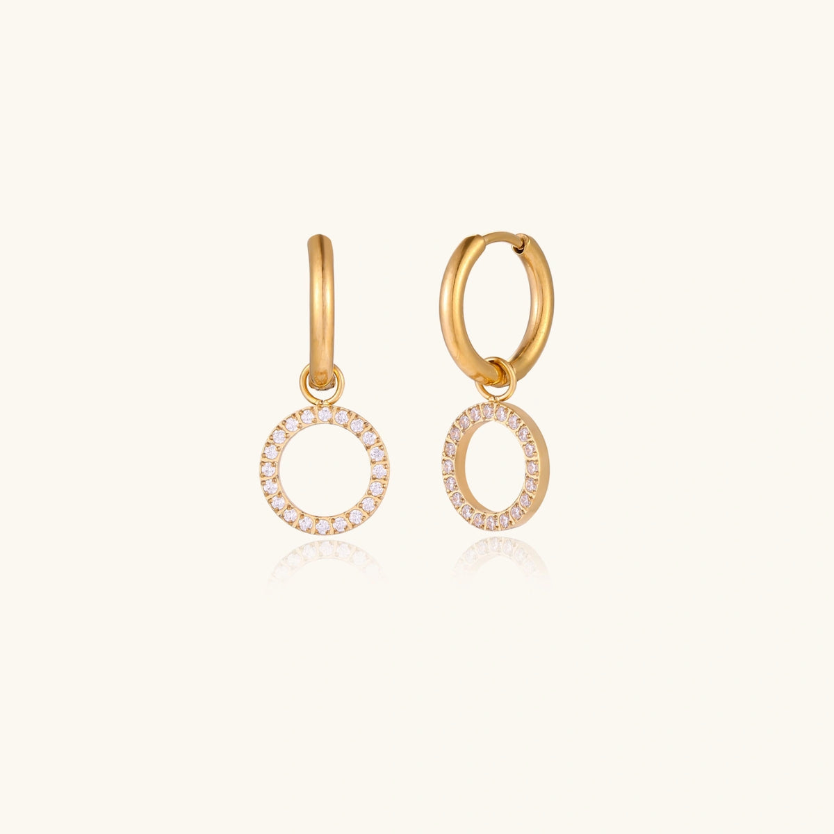 Gold-plated huggie hoop earrings with CZ-studded open circle charms on beige background