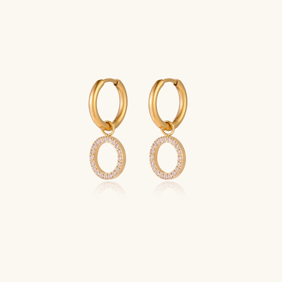 Gold-plated huggie hoop earrings with CZ-studded open circle charms on beige background