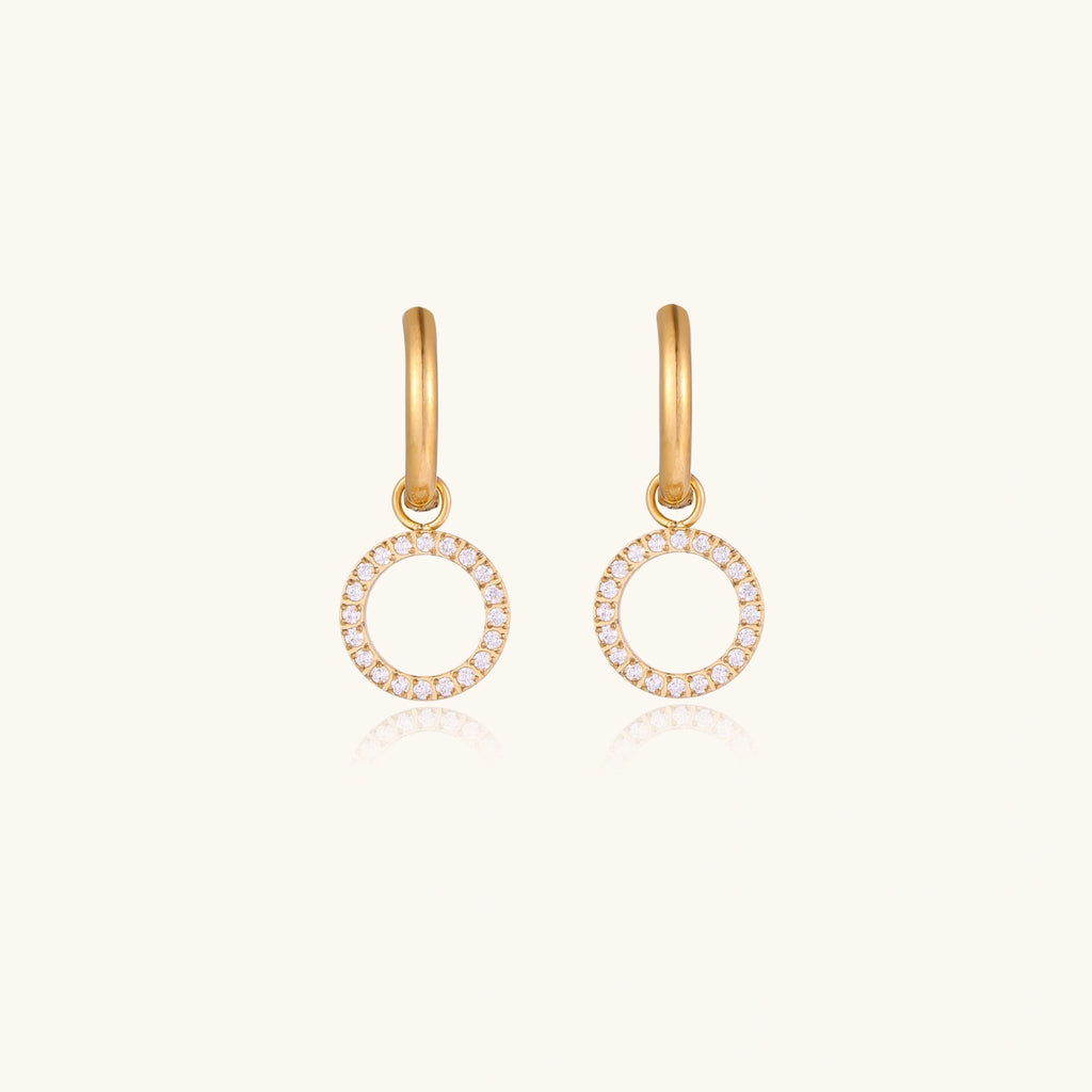 Gold-plated huggie hoop earrings with CZ-studded open circle charms on beige background