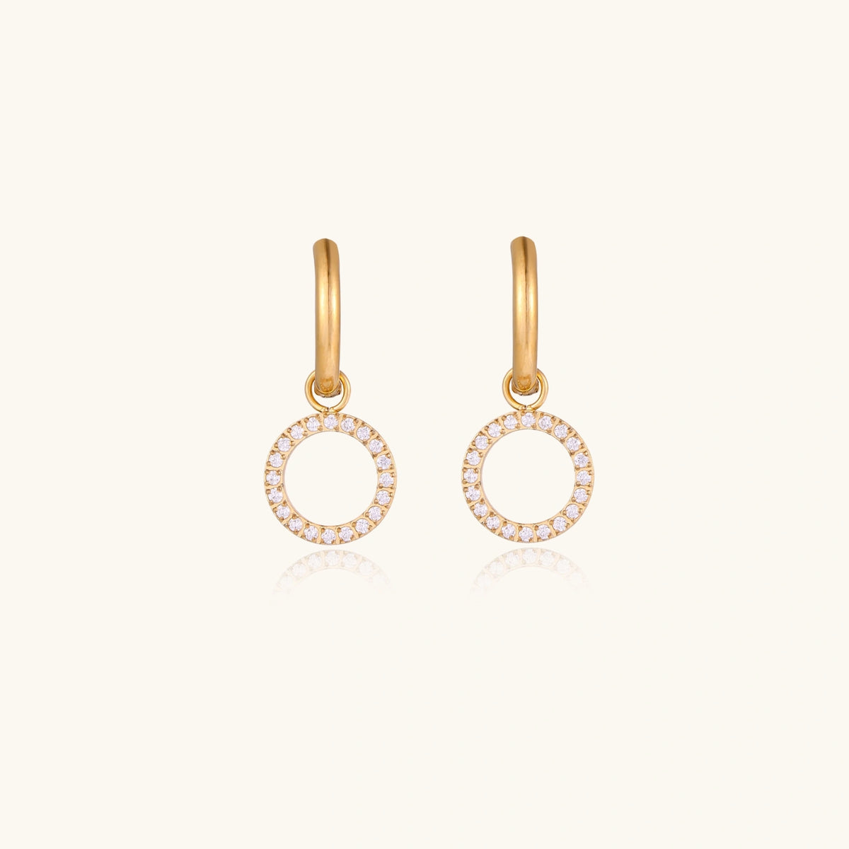 Gold-plated huggie hoop earrings with CZ-studded open circle charms on beige background