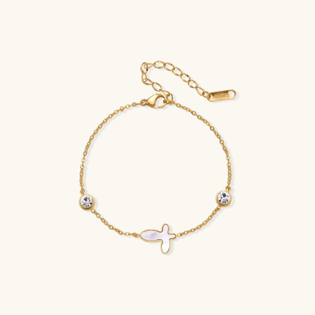 Gold chain bracelet with white mother of pearl butterfly pendant and two bezel-set crystals on cream background
