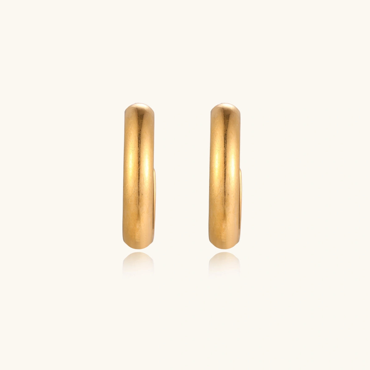 Chunky tubular hoop earrings in warm 14K gold-plated finish with smooth polished surface on cream background.