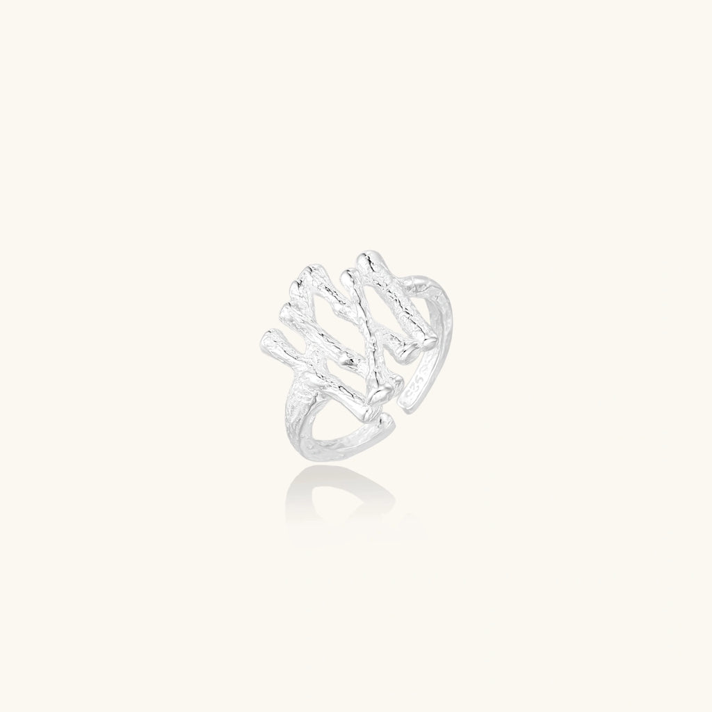 Sculptural sterling silver ring with organic branch design and textured surfaces on cream background