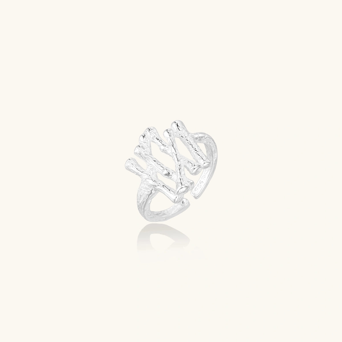 Sculptural sterling silver ring with organic branch design and textured surfaces on cream background