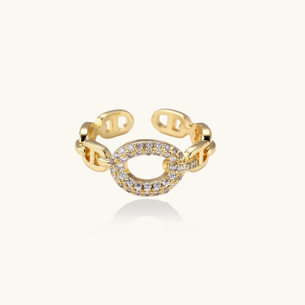 Gold-plated brass chain link ring with one oval CZ-pavé segment on cream background, adjustable cuff style.